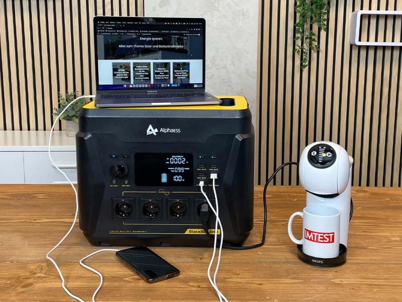 Ein Laptop, ein Smartphone und eine Kapsel-Kaffeemaschine sind an der AlphaESS BlackBee 2000 angeschlossen.