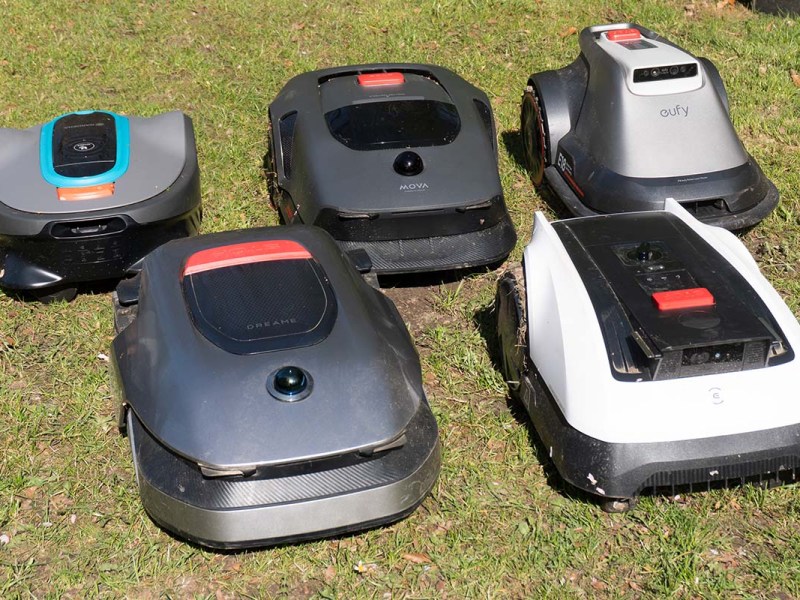 fünf Mähroboter stehen auf einem Rasen beieinander
